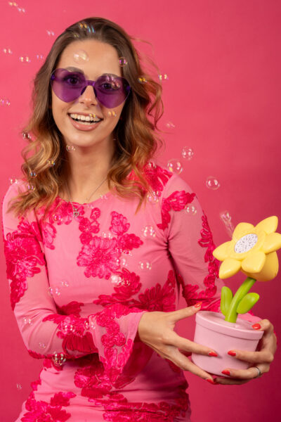 Aura ride con un vaso di fiori finti in mano tra le bolle di sapone, fondale rosa