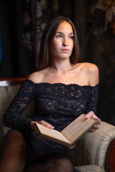 Carolina in poltrona con un libro aperto, spalle scoperte e sfondo scuro
