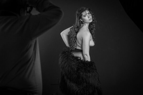 Dietro le quinte del modelsharing: un fotografo in primo piano scatta a Elena Sartori, di schiena con una pelliccia nera