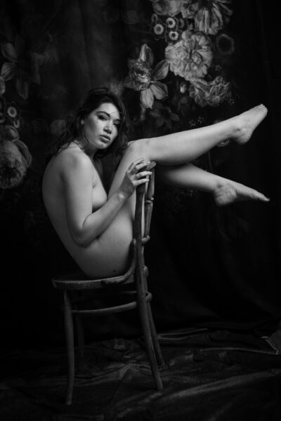 Nudo artistico: Elena Sartori sulla sedia di legno con una gamba alzata, in bianco e nero