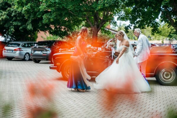 Sposa scende da un'auto d'epoca rossa aiutata da un'invitata